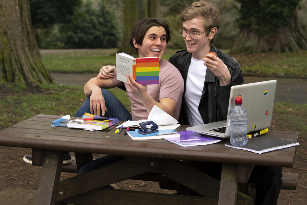 LGBTQ+ couple reading an LGBTQ+ book together while studying outdoors.