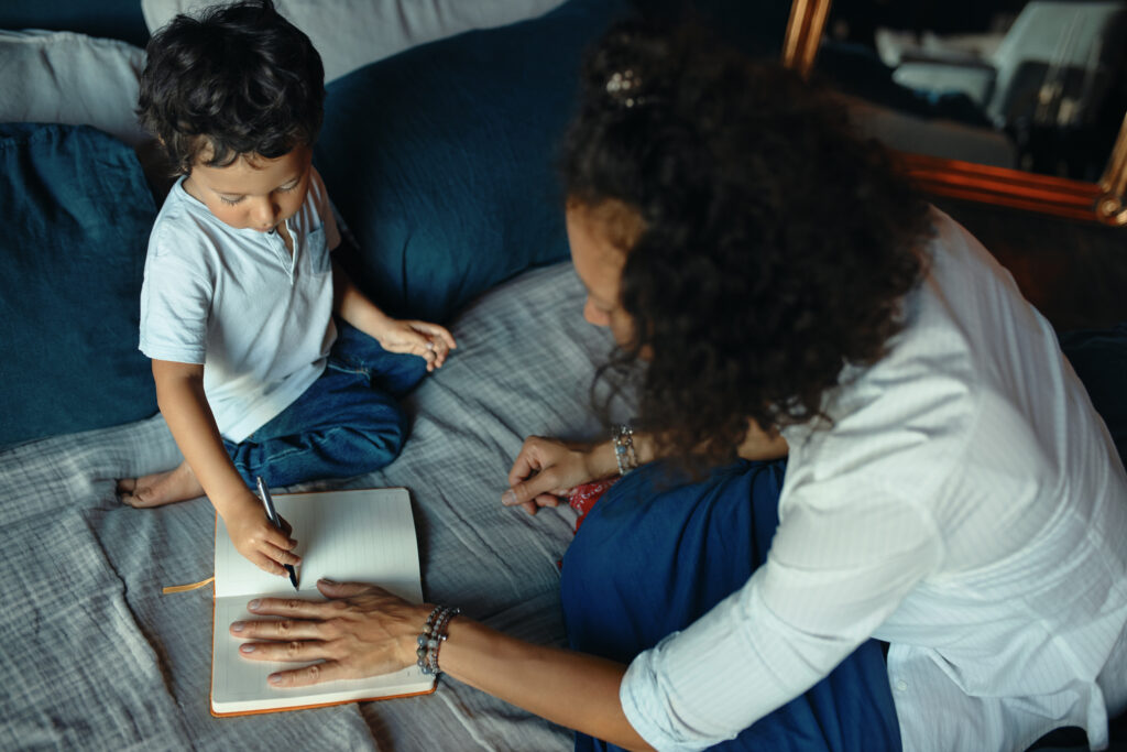 Mother helping her young child with writing and drawing at home