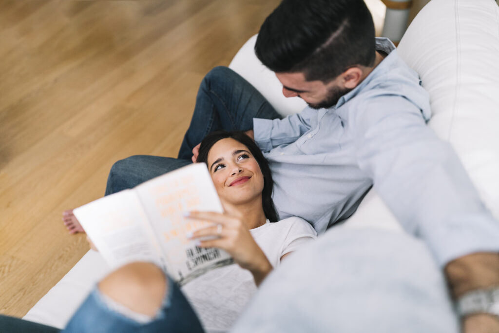 A couple spends a relaxed moment together, with the woman reading while resting beside her partner.