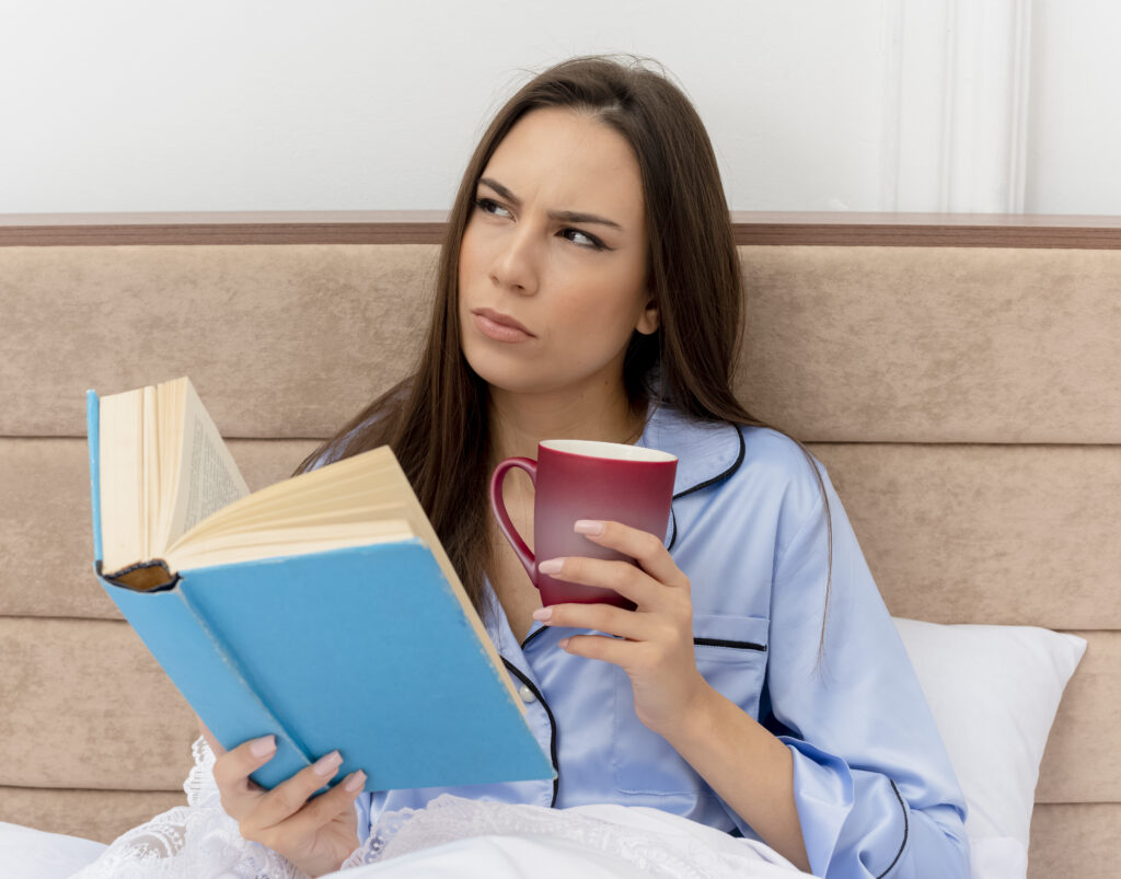 Woman reading a book in bed while reflecting on her thoughts and emotions.